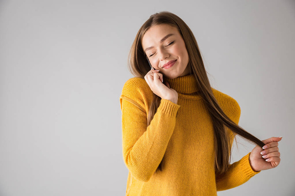 Happy young woman isolated over grey wall background talking by mobile phone. - 写真・画像