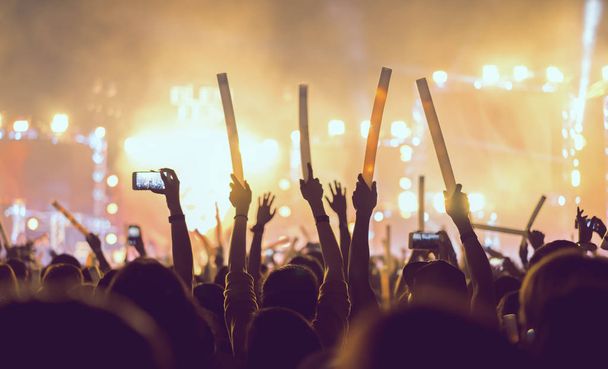 コンサート舞台照明と人々 のシルエット群衆の手を上げる観客のファンや音楽祭リア ビューでメモリースティックをグロー  - 写真・画像