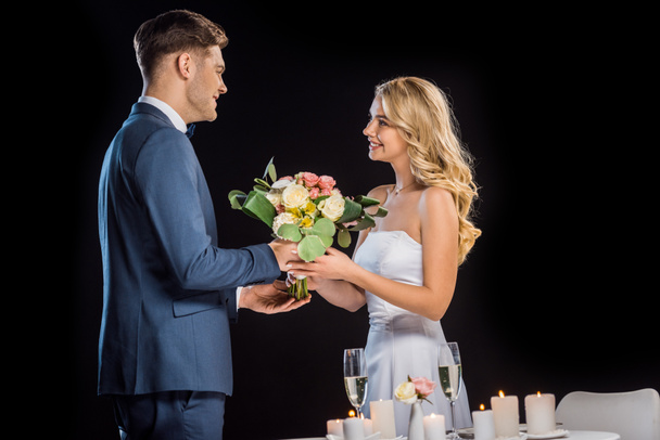 sposo sorridente presentando bouquet da sposa felice isolato su nero
 - Foto, immagini