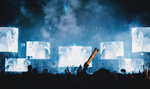 Silhouet menigte van concert podium verlichting en mensen fan publiek verhogen handen of gloed stok in het muziek festival achteraanzicht  - Foto, afbeelding