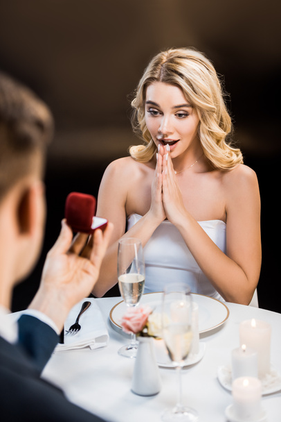 selective focus of man making marriage proposal to surprised girl on black background - Fotó, kép