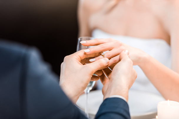 επιλεκτική εστίαση του ανθρώπου βάζοντας το γαμήλιο δαχτυλίδι στο δάχτυλο νύφες σε μαύρο φόντο - Φωτογραφία, εικόνα