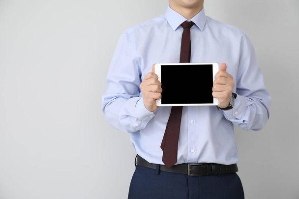 Young businessman with tablet PC on light background - Foto, imagen