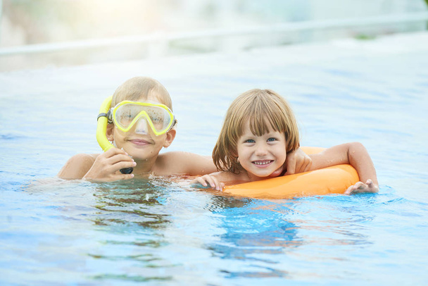 Neşeli kardeşler şişme halkalı ve şnorkel yüzme havuzunda yaz gün harcama - Fotoğraf, Görsel