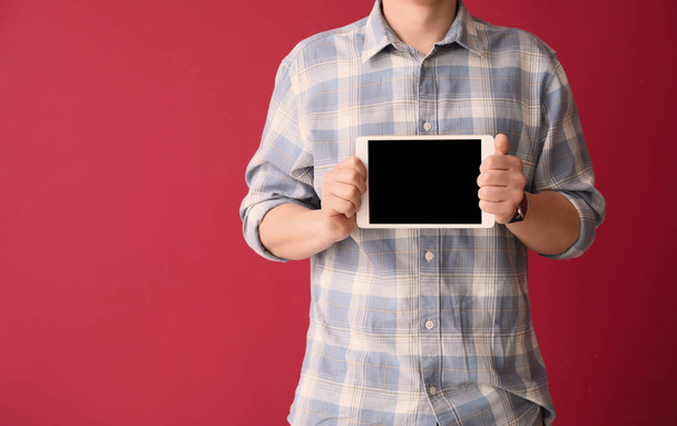 Young businessman with tablet PC on color background - Fotó, kép