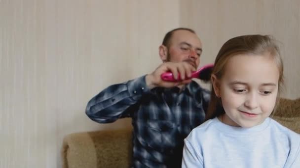 Dad combs his daughters hair while sitting on the couch. Dad and daughter spend time together. - Materiaali, video