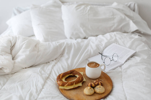 Bagel with cheese, homemade cookies and coffee served on wooden tray on bed - Photo, Image
