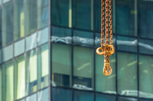 Gancio in metallo sulla catena dalla gru di costruzione sullo sfondo di un vetro da costruzione moderno
 - Foto, immagini