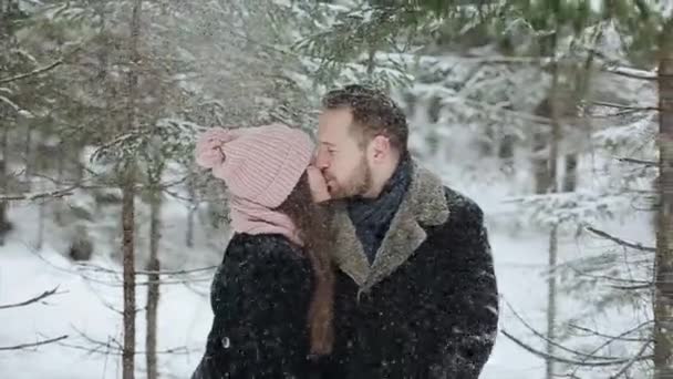 Joven hermosa pareja caucásica besándose bajo una nieve en un bosque de invierno. Los millennials a la moda se divierten juntos. Imágenes sinceras de parejas jóvenes en el bosque. Movimiento lento
. - Metraje, vídeo