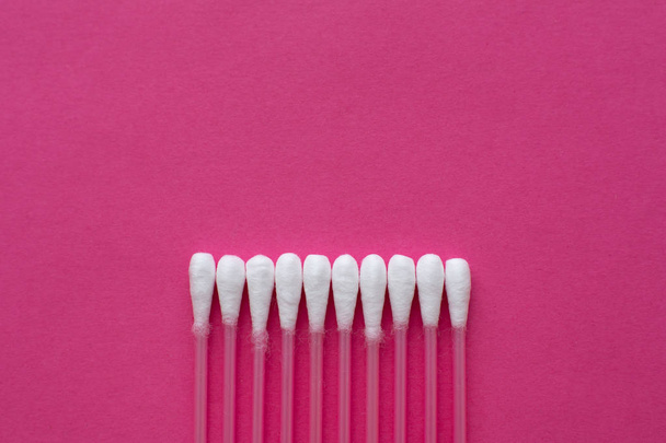 Closeup top view on cotton buds laid in a horizontal line on pink background - Foto, Bild