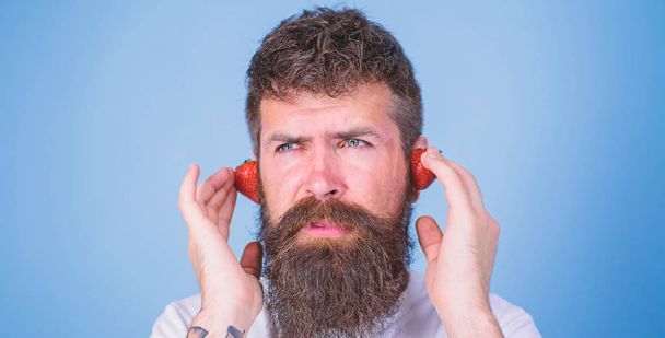 Summer top radio chart. Man bearded hipster red ripe strawberry ears as headphones. Summer hit concept. Guy enjoy juicy sound summer hit song music. Hipster beard listen music strawberry earphones - Fotoğraf, Görsel