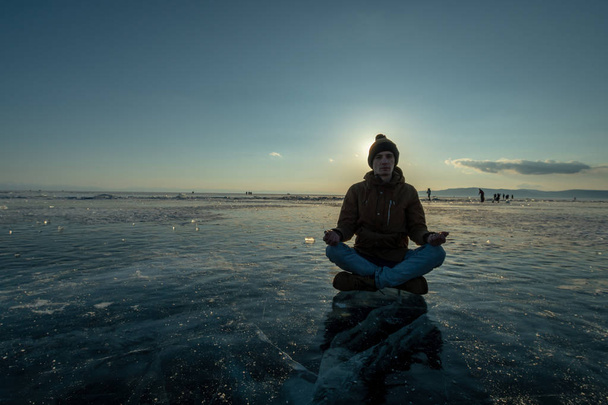 Tourist with a backpack meditates sitting in Lotus position on the ice of lake Baikal. Relaxation and freedom of nature - Foto, Imagem