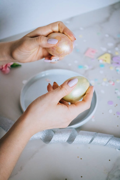 Girl breaks golden easter eggs on marble background, confetti, sparkles, ribbons. - Фото, изображение