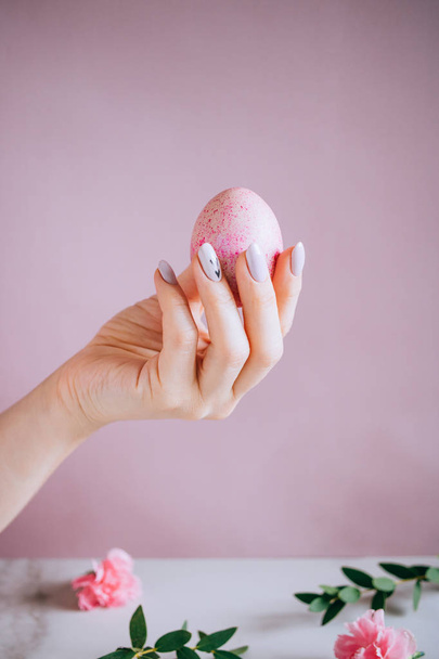 The girl is holding in hand a pink easter egg, pink and marble background, minimalism, flowers - Foto, imagen
