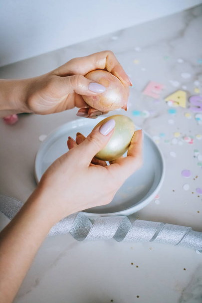 Girl breaks golden easter eggs on marble background, confetti, sparkles, ribbons. - Foto, Imagem