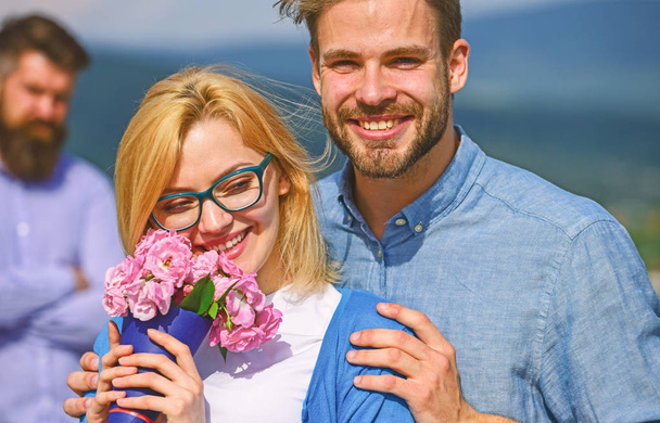 Lovers hugs outdoor flirt romance relations. Couple in love dating while jealous bearded man watching wife cheating him with lover. Infidelity concept. Couple romantic date lovers bouquet flowers - Zdjęcie, obraz