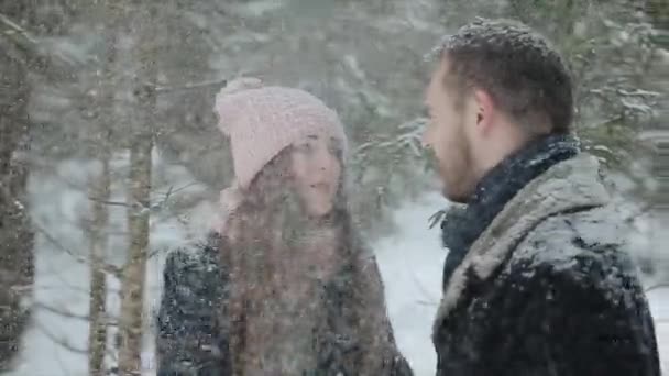 Молодая красивая кавказская пара целуется под снегом в зимнем лесу. Модные миллениалы веселятся вместе. Открытые кадры молодой пары в лесу. Медленное движение
. - Кадры, видео