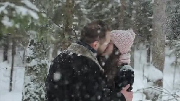 Jonge mooie Kaukasische paar zoenen onder een sneeuw in een winter forest. Modieuze millennials plezier toghether. Candid beelden van jong koppel in bos. Slow motion. - Video