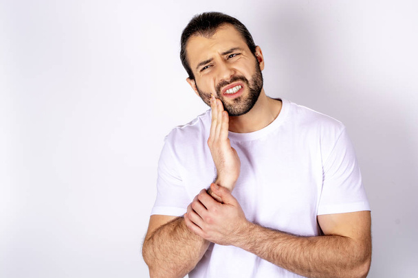 Pohledný muž v bílém tričku na bílém pozadí, bolest zubů - Fotografie, Obrázek