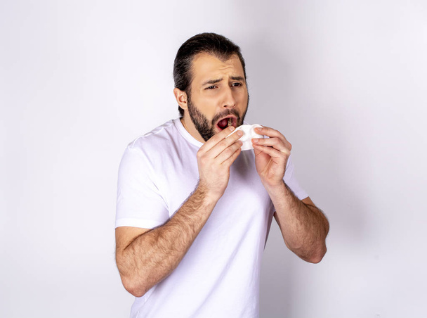 schöner Mann in weißem T-Shirt vor weißem Hintergrund, niest, erkältet - Foto, Bild