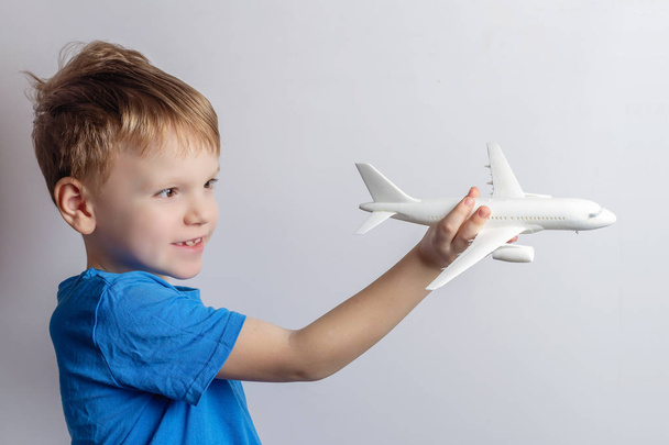 Um menino de seis anos brinca com um modelo de brinquedo de um avião de passageiros. Conceito de sonho de viagem
 - Foto, Imagem