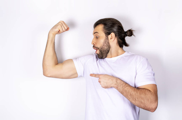 Handsome man in white t-shirt on white background, shows biceps, strong arms - Fotó, kép