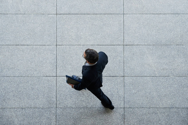 Бизнесмен с папкой шагает по плиточному полу, вид сверху
 - Фото, изображение
