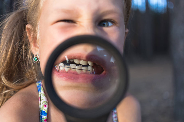 Mała dziewczynka położyć szkło powiększające usta, by pokazać ort - Zdjęcie, obraz