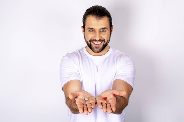 Un hombre guapo con una camiseta blanca sobre un fondo blanco, sonriendo, sosteniendo pastillas en su mano
 - Foto, imagen