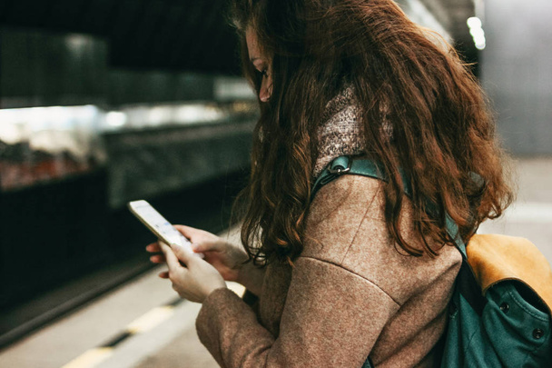 Giovane donna riccia rossa viaggiatore testa ragazza con zaino utilizzando cellulare in metropolitana
 - Foto, immagini