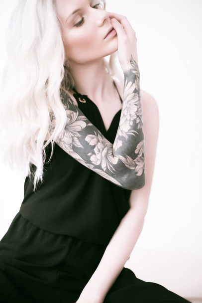 Attractive girl with blond hair and a tattoo on her arm   in a black shirt - Фото, изображение