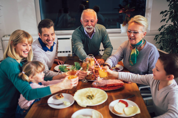 Monen sukupolven perhe nauttii ateriasta ympäri pöytää kotona
  - Valokuva, kuva