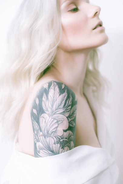 Attractive girl with blond hair and a tattoo on her arm in a white shirt - Foto, Imagen