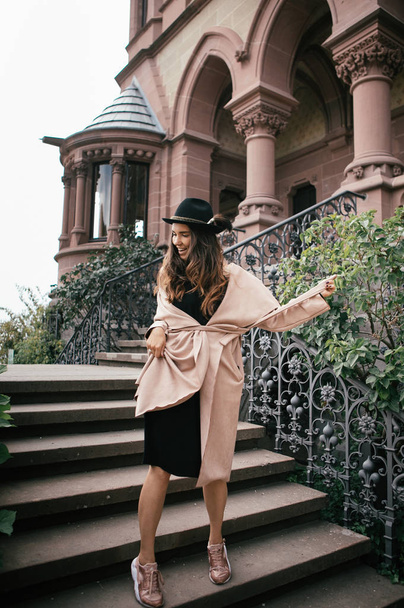 Sexy girl in black dress, pastel pink coat and hat posing at the medieval castle - Φωτογραφία, εικόνα