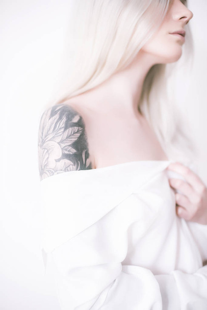 Attractive girl with blond hair and a tattoo on her arm in a white shirt - Foto, afbeelding