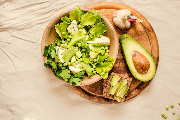 Fresh delicious green salad with avocado in a wooden plate and g - 写真・画像