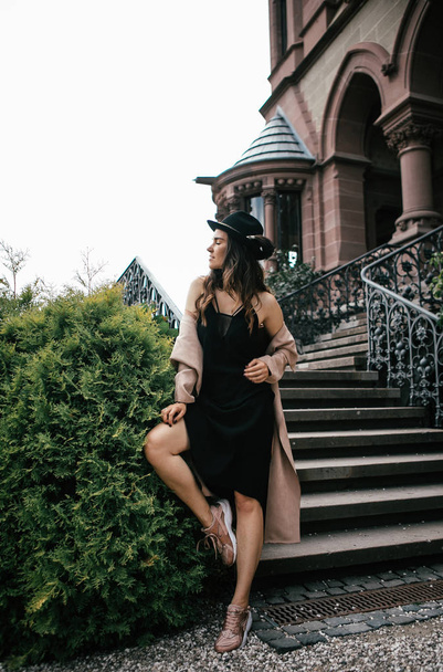 Sexy girl in black dress, pastel pink coat and hat posing at the medieval castle - Φωτογραφία, εικόνα