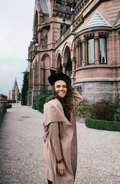 Sexy girl in black dress, pastel pink coat and hat posing at the medieval castle - Fotó, kép