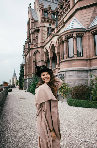 Sexy girl in black dress, pastel pink coat and hat posing at the medieval castle - Photo, Image