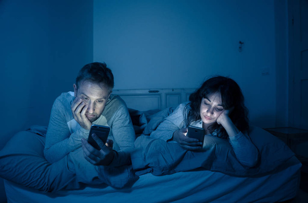 Life style portrait of young bored couple in bed at night on smart phones obsessed with games, social media, apps ignoring each other. Relationship communication problems and phone addiction concept. - Photo, Image