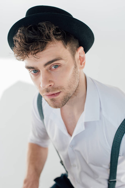 selective focus of handsome dreamy man in white shirt and black hat  - Zdjęcie, obraz