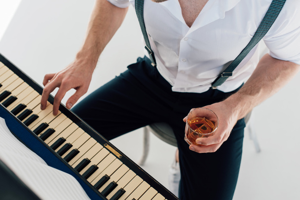 обрізаний подання піаніст, проведення келих улюбленого напою алкоголь під час гри фортепіано  - Фото, зображення