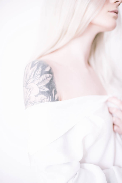 Attractive girl with blond hair and a tattoo on her arm in a white shirt - Фото, зображення