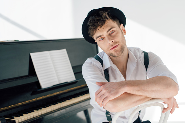 dreamy pianist in white shirt and black hat looking at camera - Foto, imagen