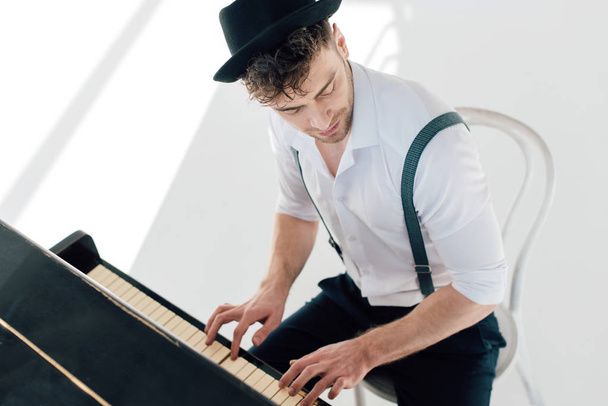 handsome musician in white shirt and black hat playing piano - Foto, Bild
