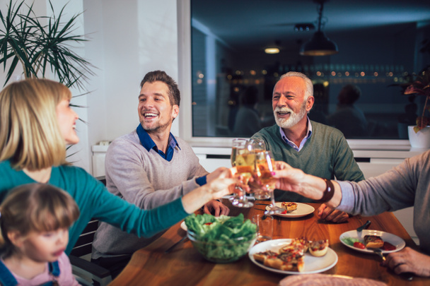 Familia multigeneracional disfrutando de la comida alrededor de la mesa en casa
  - Foto, Imagen