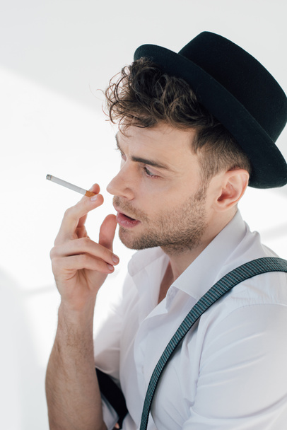 handsome man in white shirt and black hat smoking cigarette - Photo, Image