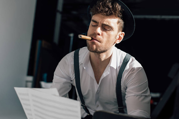 handsome musician holding music book sheets while smoking cigar - Foto, imagen
