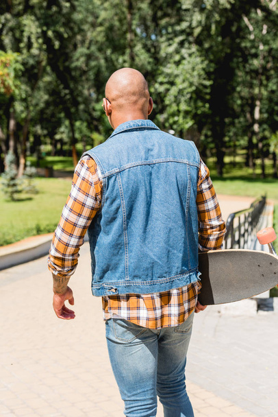back view of african american young man holding longboard in park - Foto, immagini