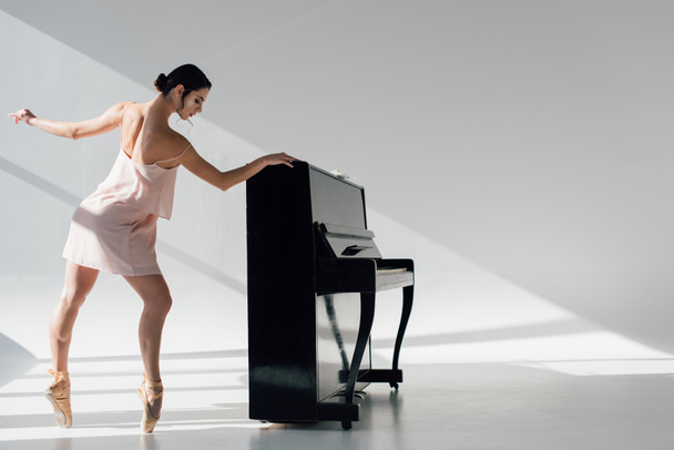 黒のピアノに近い日光で踊る美しい若いバレリーナ - 写真・画像